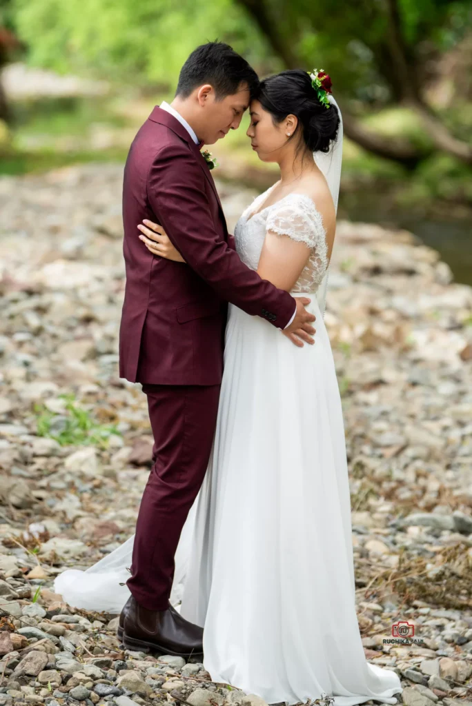 Bride and groom embracing on a rocky riverside, sharing an intimate moment outdoors.