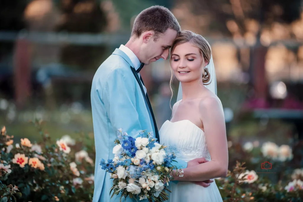 Bride and groom embracing outdoors in a garden with flowers, smiling gently