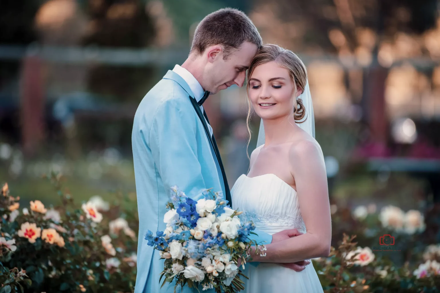 Bride and groom embracing outdoors in a garden with flowers, smiling gently