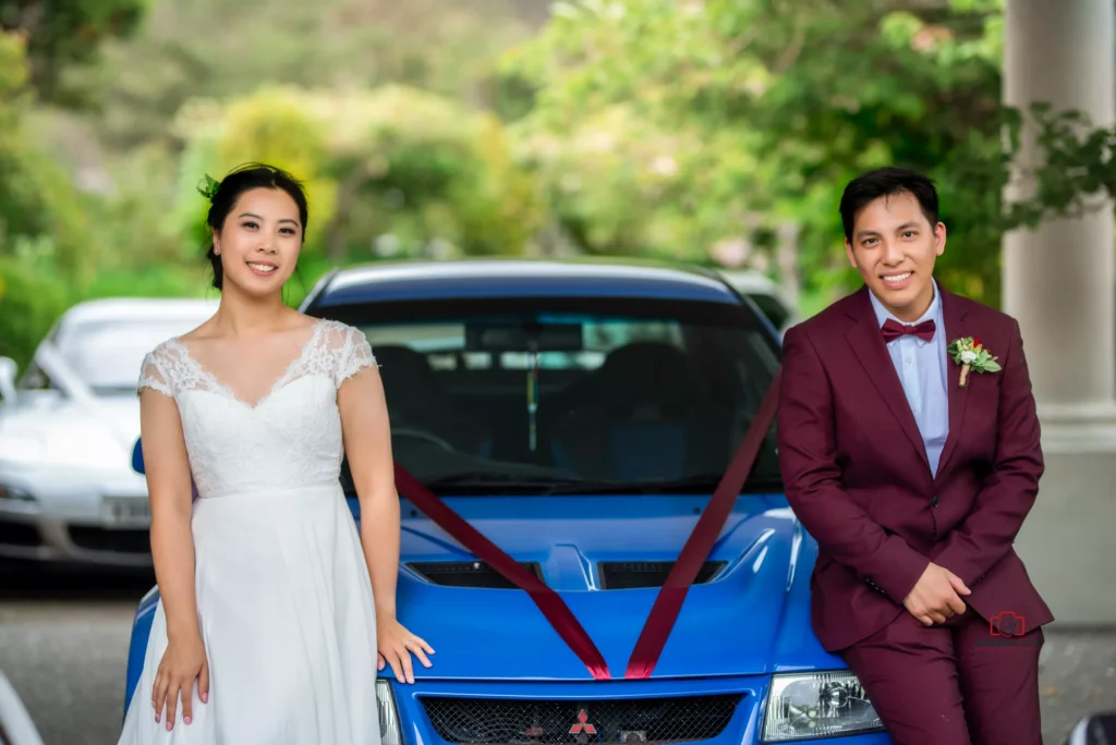 Bride and groom posing with a blue car decorated with ribbons on their wedding day