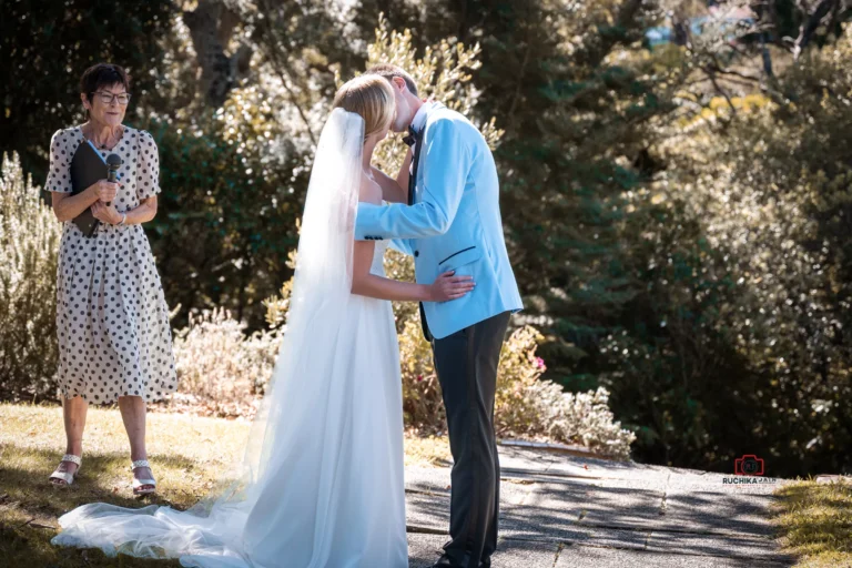 Bride and groom sharing a kiss outdoors during their wedding ceremony, with an officiant standing nearby