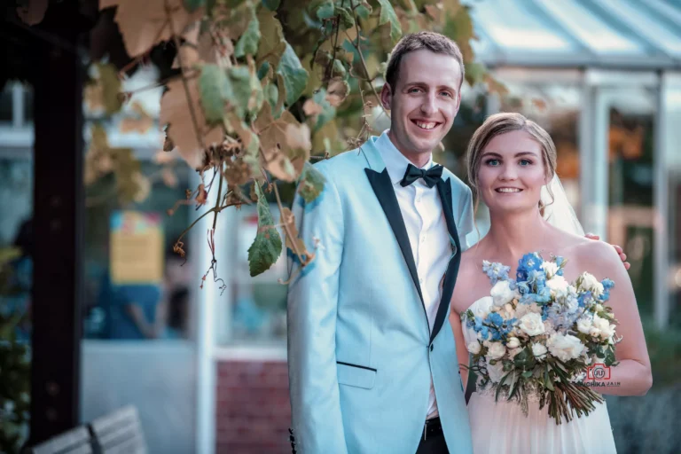 Bride and groom smiling and posing outdoors with a bouquet of blue and white flowers