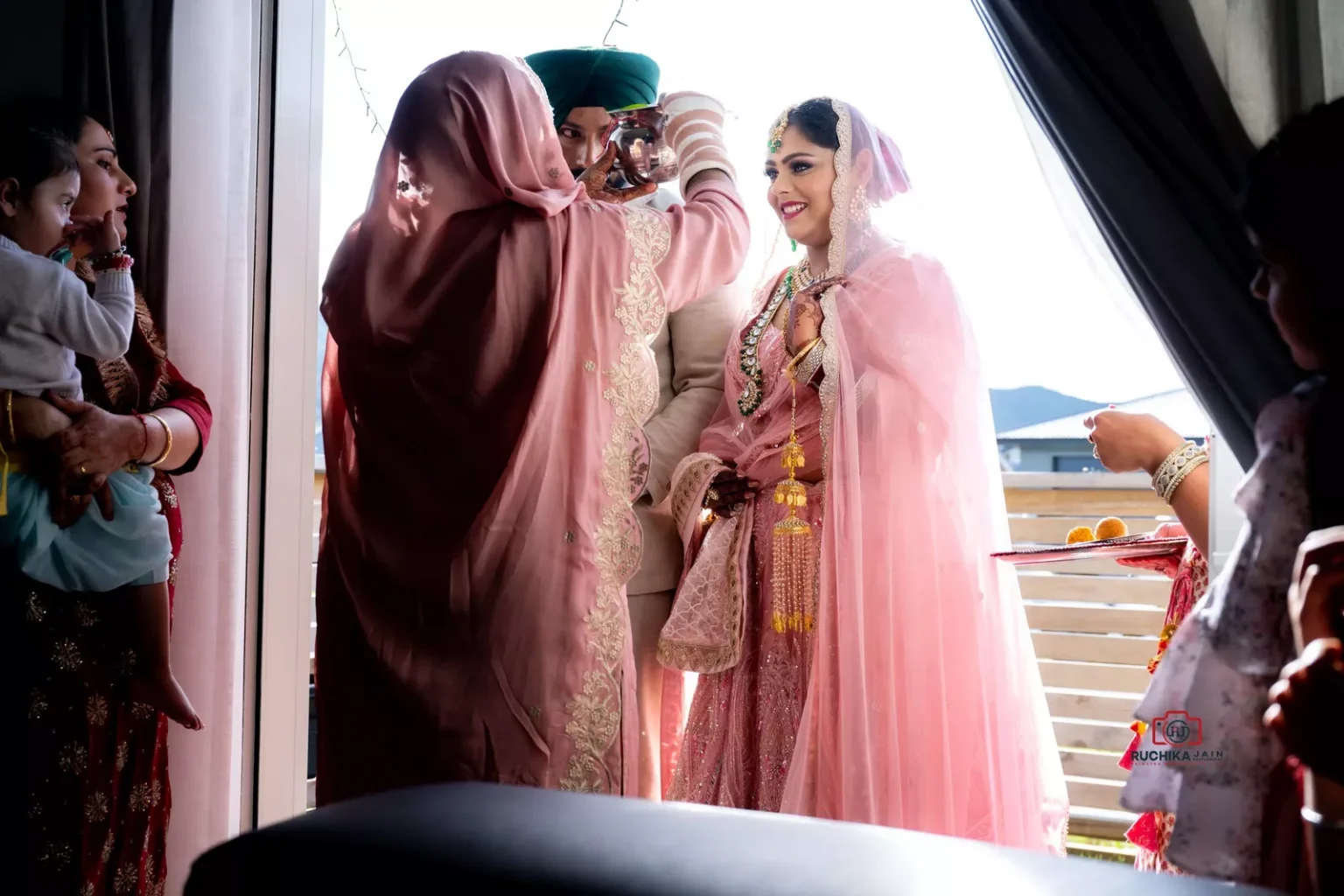 Bride and groom standing in a doorway as a woman performs a traditional welcome ceremony inside a house