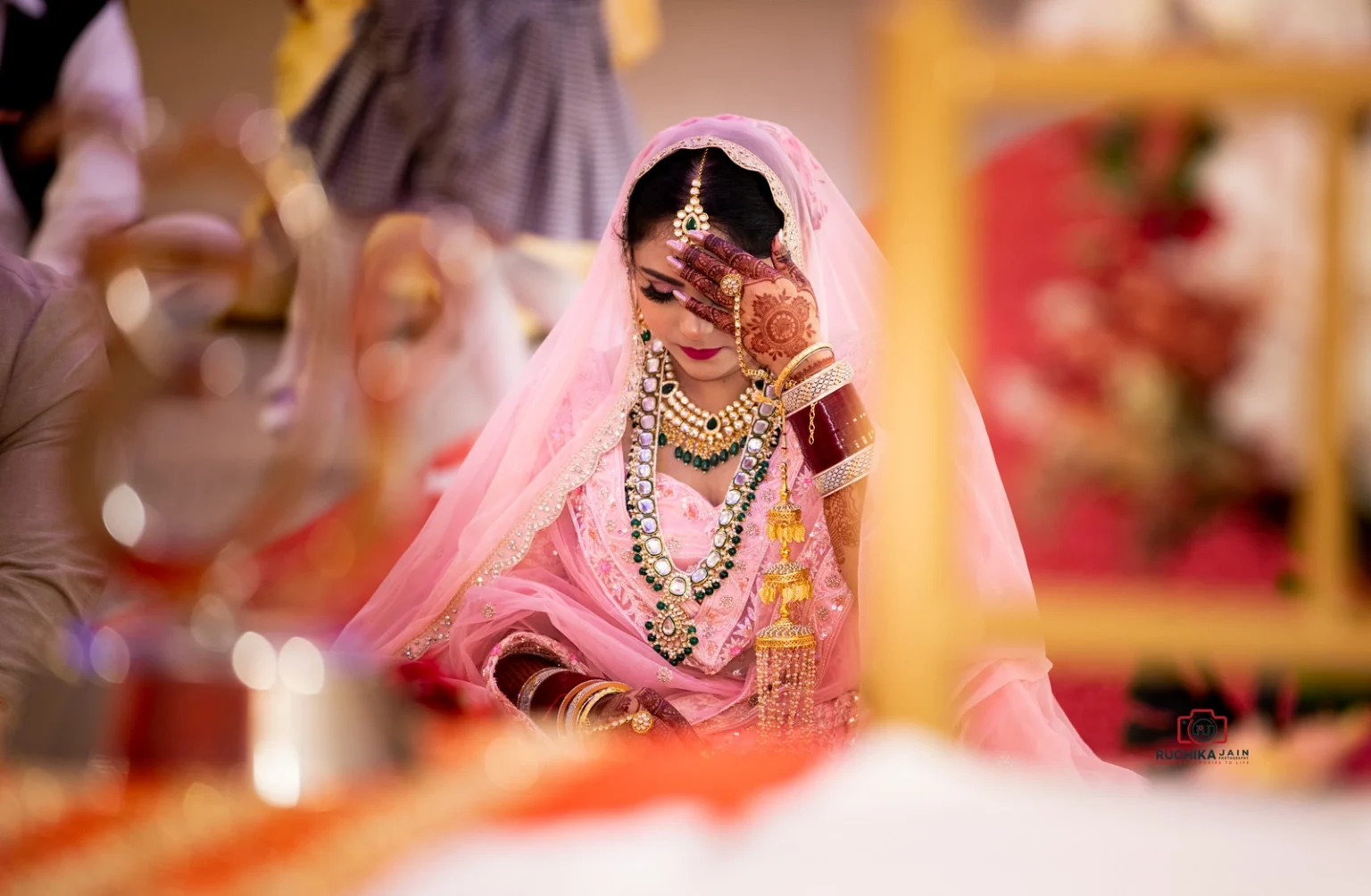 Bride covering her face during a Sikh wedding ceremony, dressed in pink lehenga with intricate jewelry