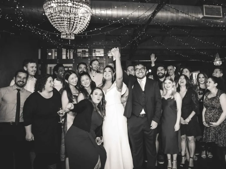 Bride and groom celebrating with a group of friends and family under twinkling lights and chandeliers