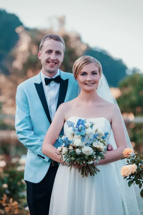 Bride holding a bouquet with groom standing behind her outdoors