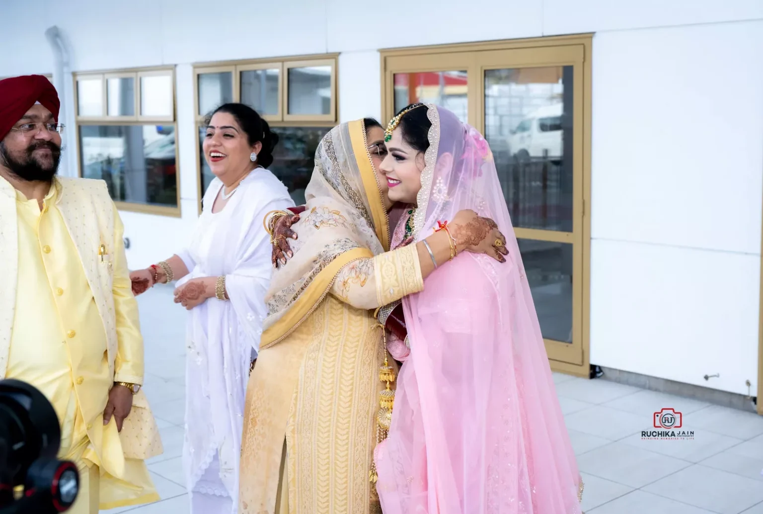 Bride hugs a family member outside a Sikh wedding venue, while others look on and smile