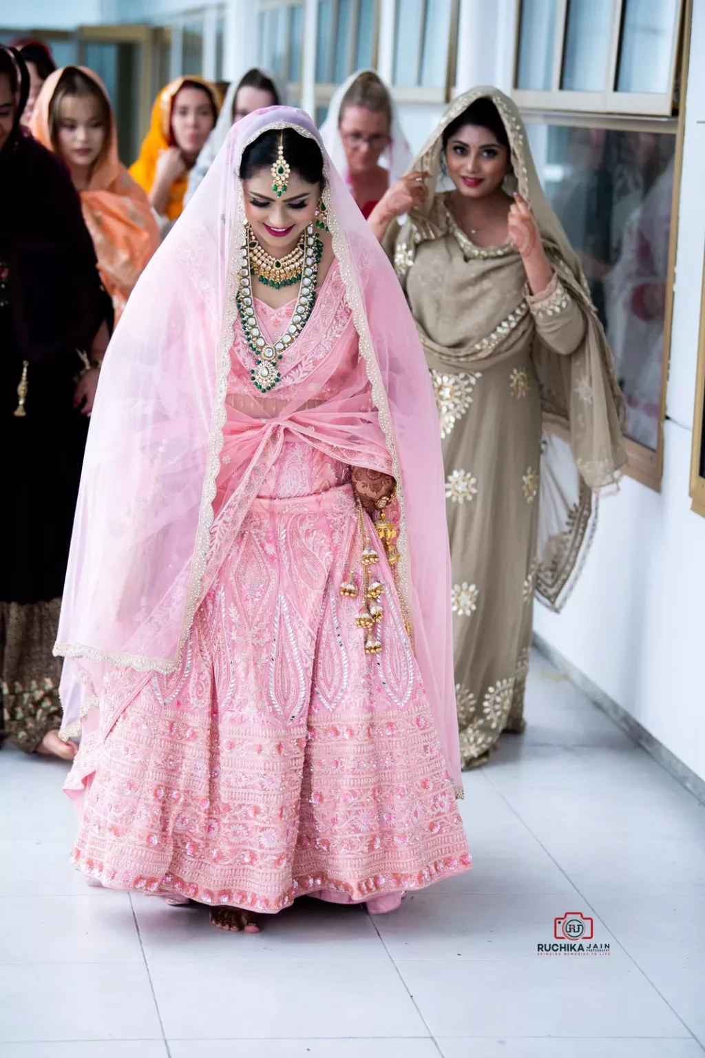 Bride in a pink lehenga walking with bridesmaids during a Sikh wedding ceremony