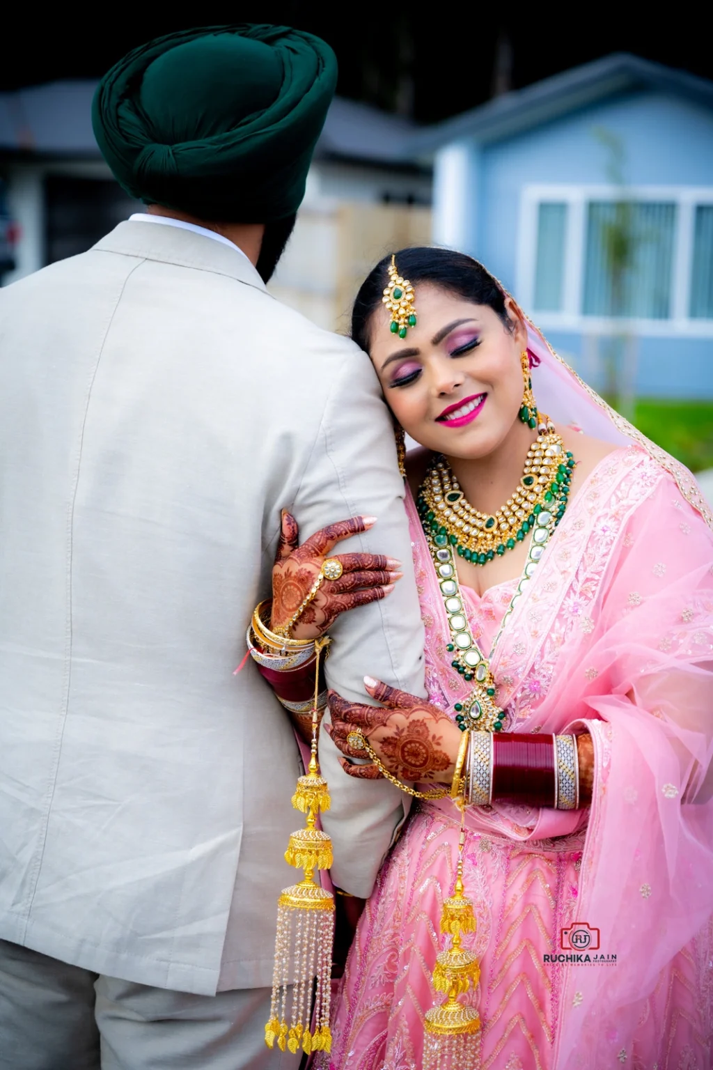 Bride in pink dress with henna and jewelry leaning on groom in beige suit outdoors