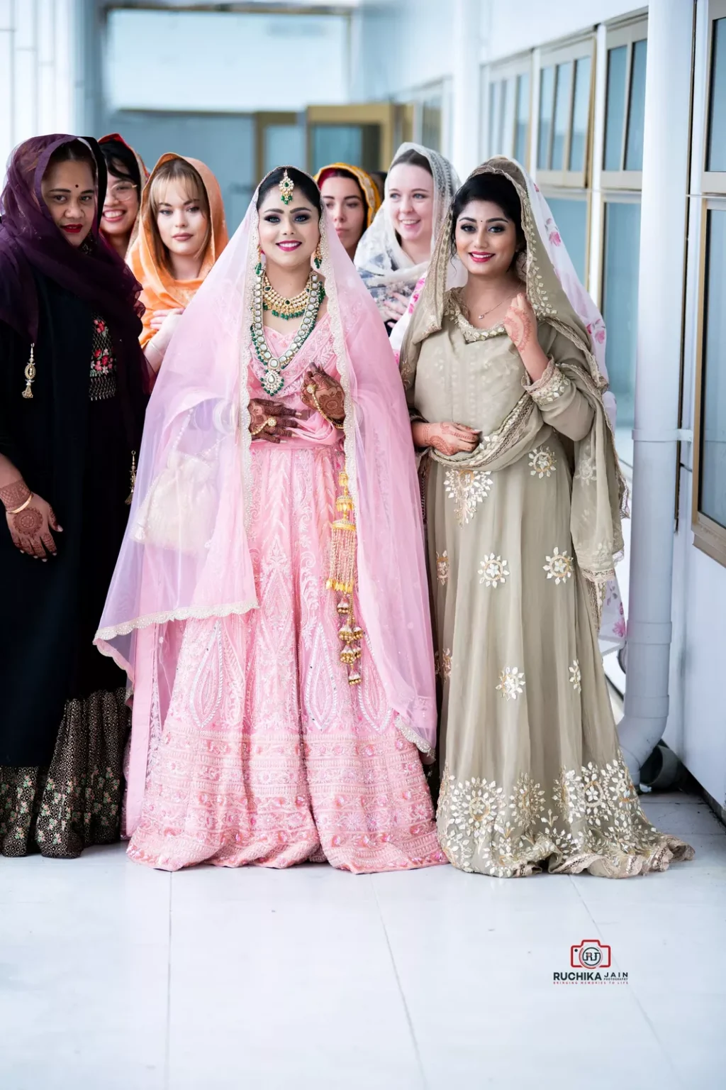 Bride in pink traditional attire posing with bridesmaids in colorful dresses during a Sikh wedding