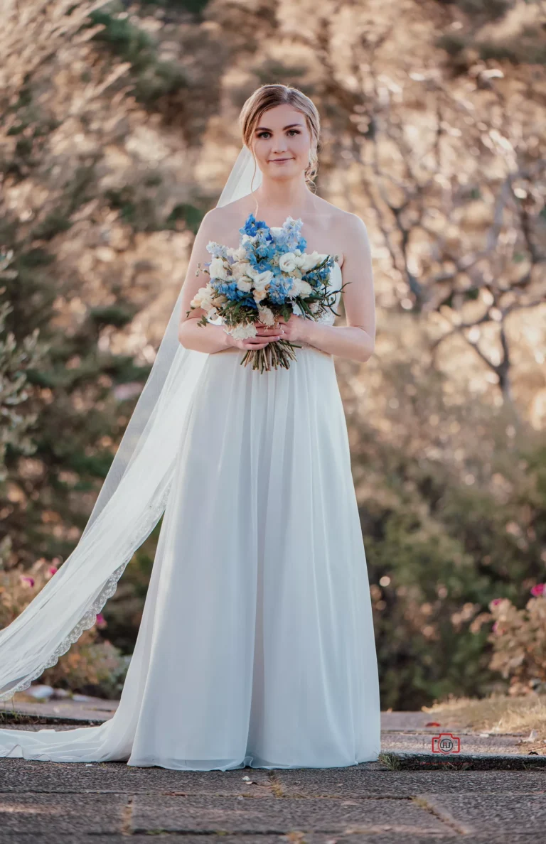 Bride in white dress holding a blue and white bouquet with a natural outdoor background