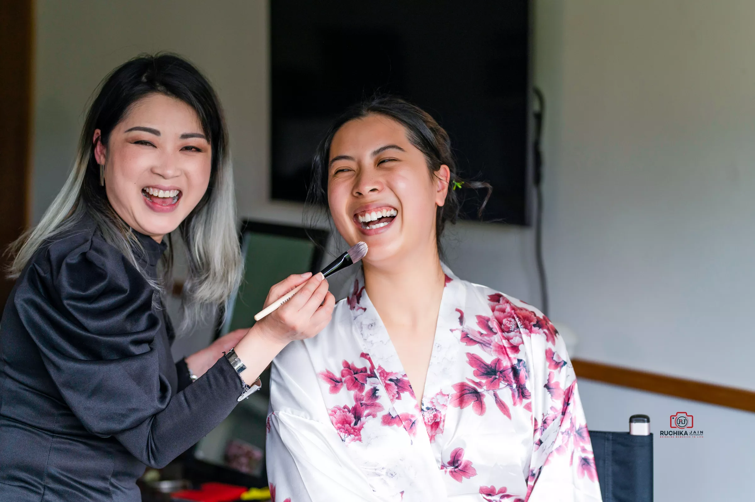 Bride laughing while getting makeup done by an artist before the wedding