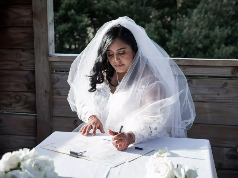 Bride signing a marriage certificate at a table with white flowers