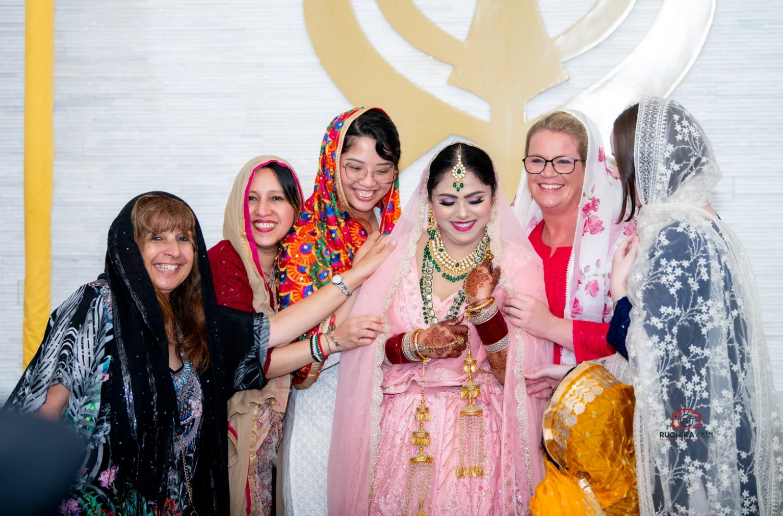 Bride surrounded by smiling friends in traditional attire at a Sikh wedding