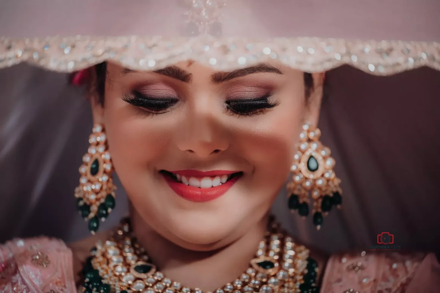 Close-up of a smiling bride wearing traditional jewelry, with a veil gently framing her face