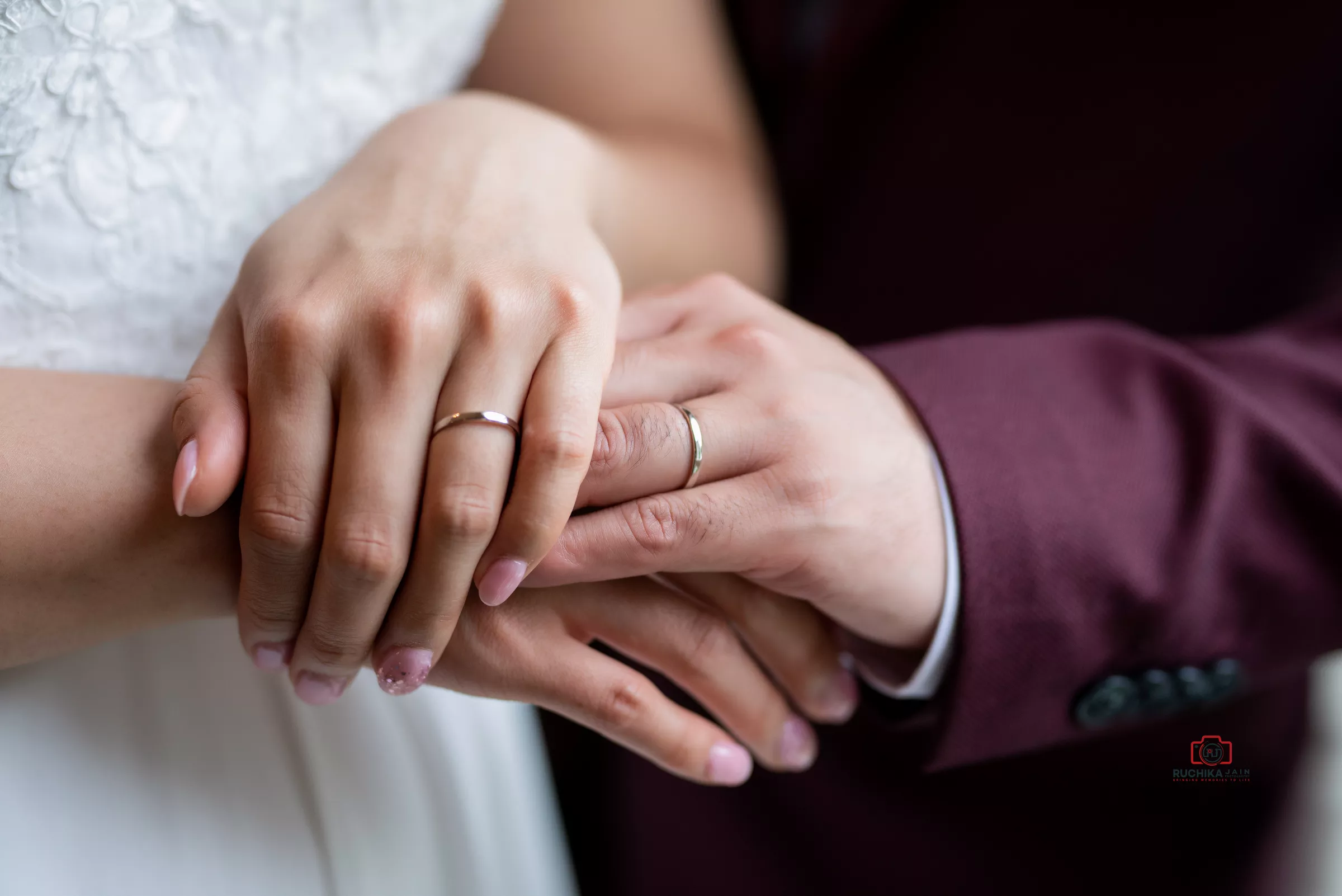 Close-up of bride and groom holding hands, showing their wedding rings