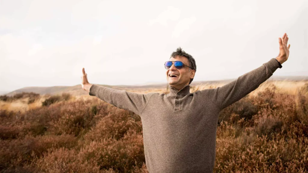 Dinesh Jain, Photographer, smiling with open arms in an outdoor landscape, wearing sunglasses