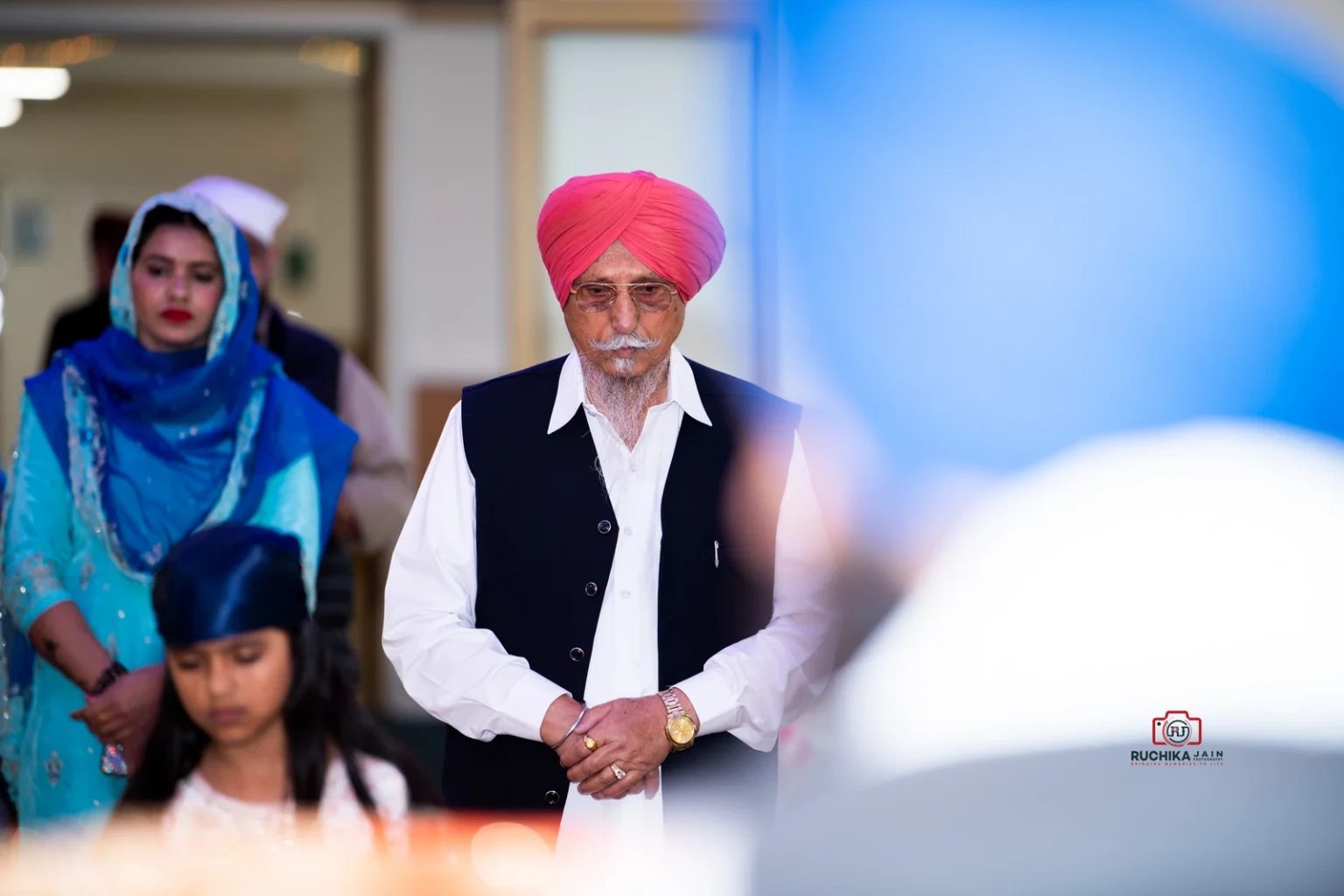 Elderly man in a pink turban and traditional attire standing solemnly during a Sikh wedding ceremony