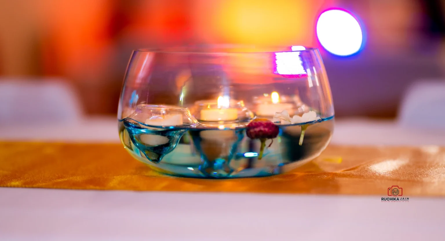 Floating candles in a glass bowl with water and flowers on a table