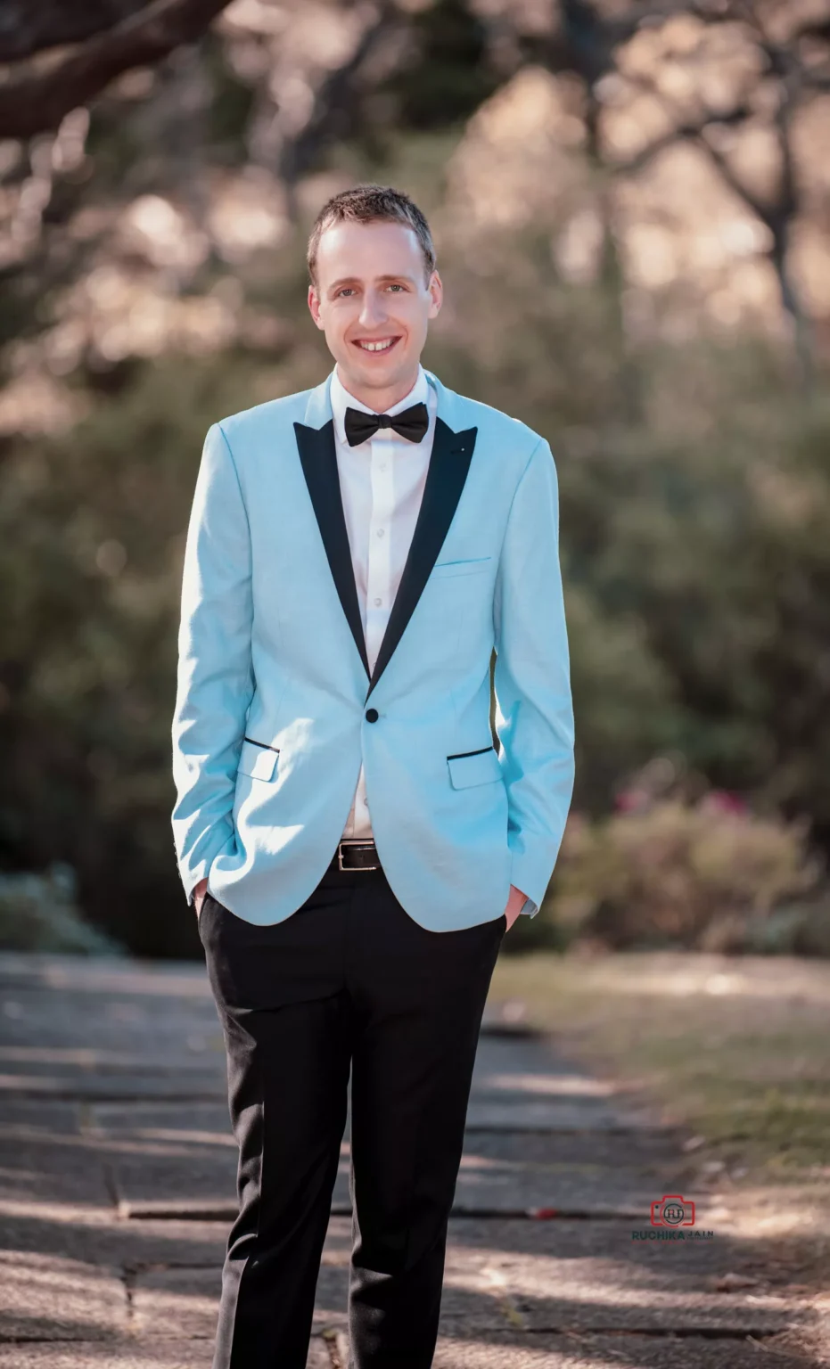 Groom in light blue tuxedo jacket with black lapels posing outdoors