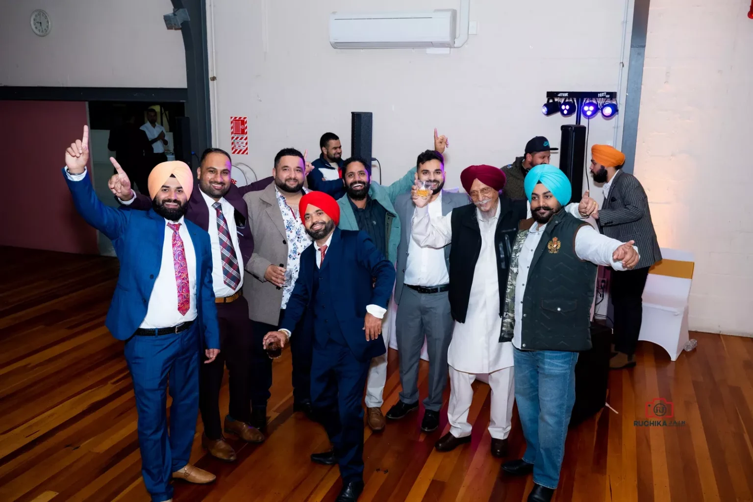 Group of men in celebratory poses at an indoor event, some holding drinks and smiling at the camera