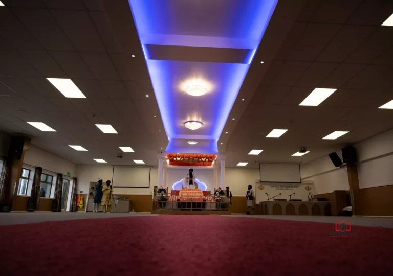 Interior of a Gurdwara with blue-lit ceiling and prayer area set up for a ceremony