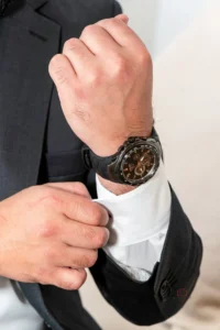 Man adjusting cuff of his white shirt while wearing a black watch