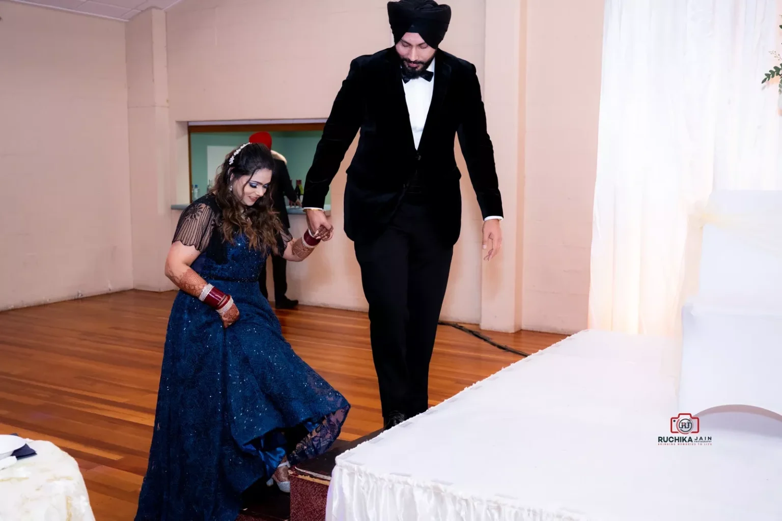 Man in black tuxedo holding woman's hand as she steps up in a navy blue dress at a formal event