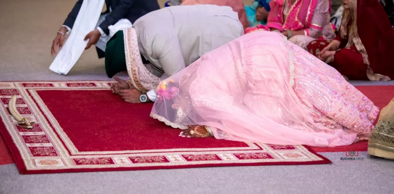 Sikh bride and groom bowing in prayer during wedding ceremony on a red mat