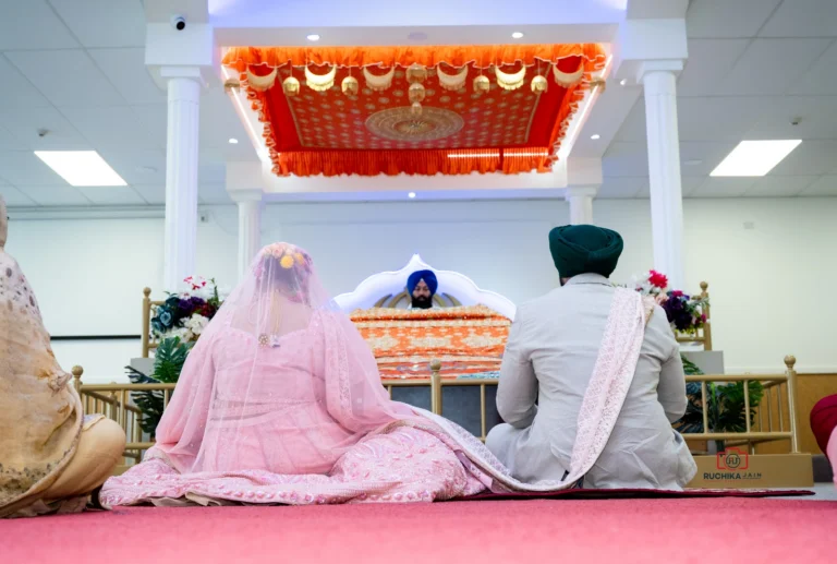 Sikh bride and groom sitting in front of the Guru Granth Sahib during their wedding ceremony in a gurdwara.