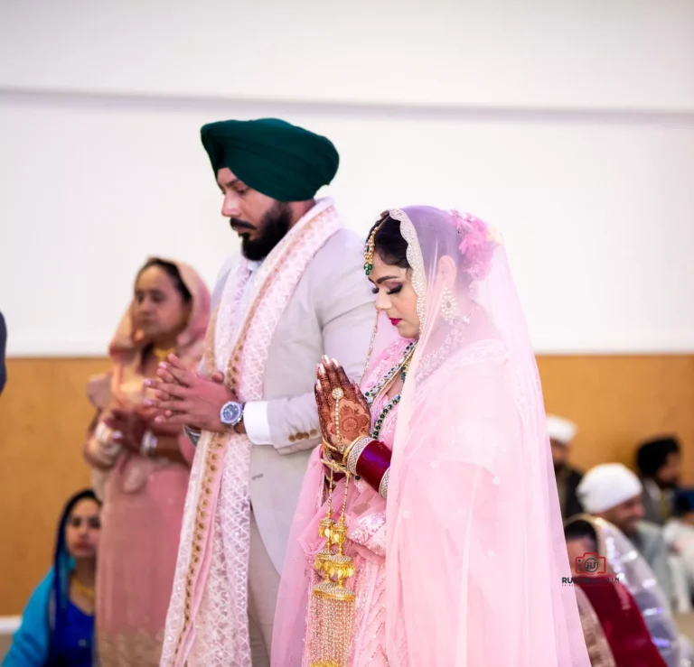 Sikh bride and groom standing with hands clasped in prayer during wedding ceremony