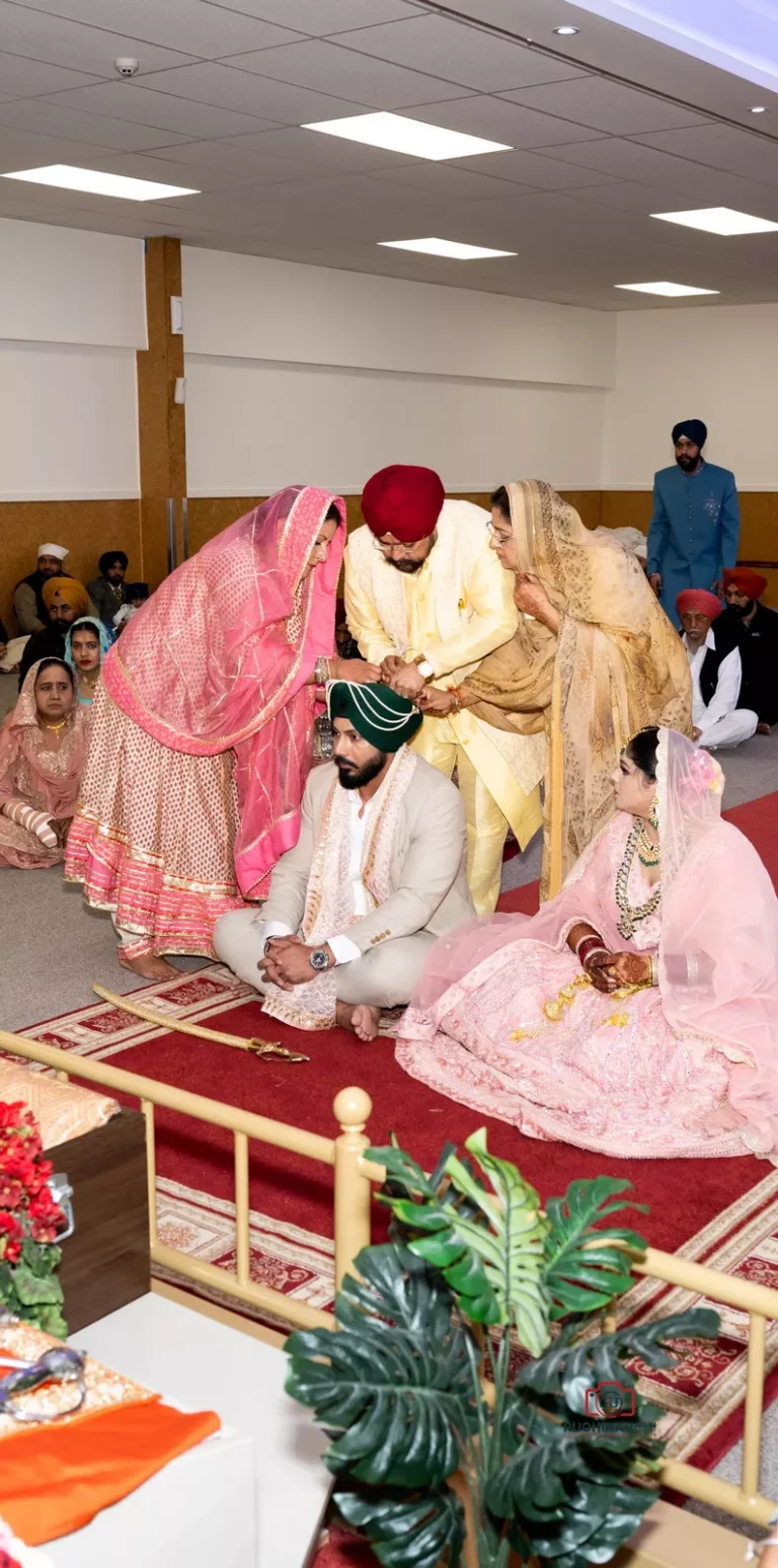 Sikh groom and bride seated during a wedding ceremony, with family members performing traditional rituals