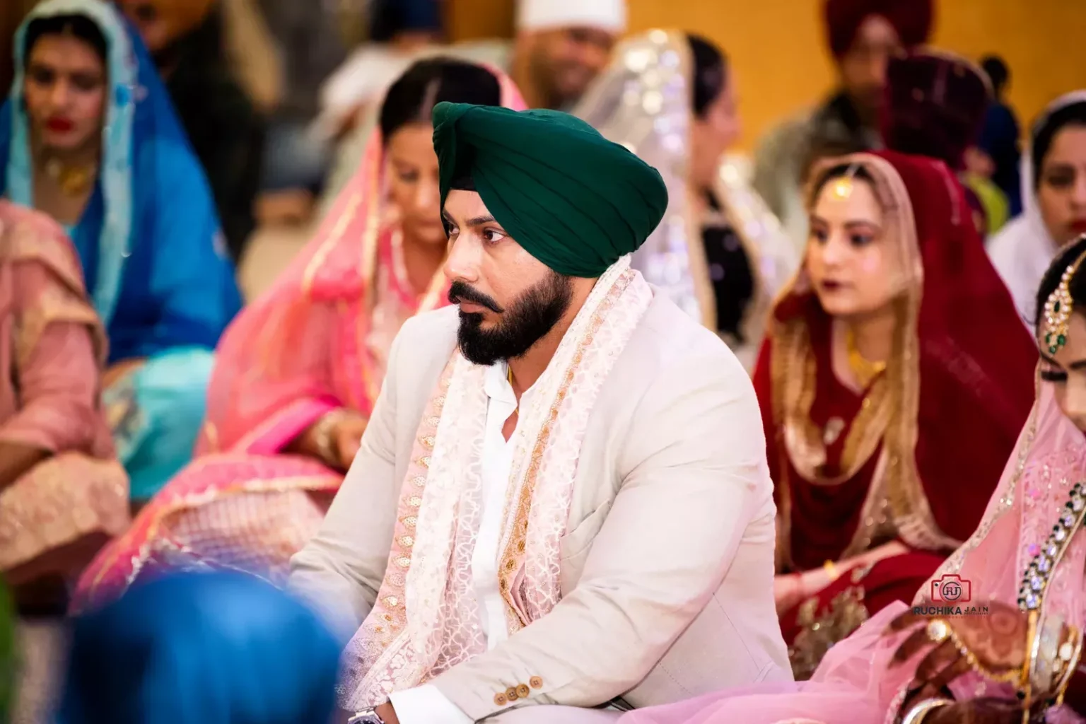 Sikh groom in a green turban seated during the wedding ceremony surrounded by family and guests