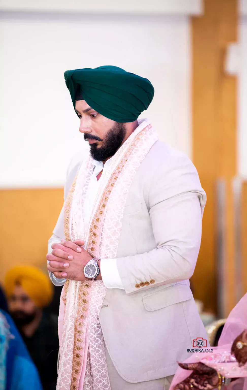 Sikh groom in traditional attire, standing with hands clasped during wedding ceremony