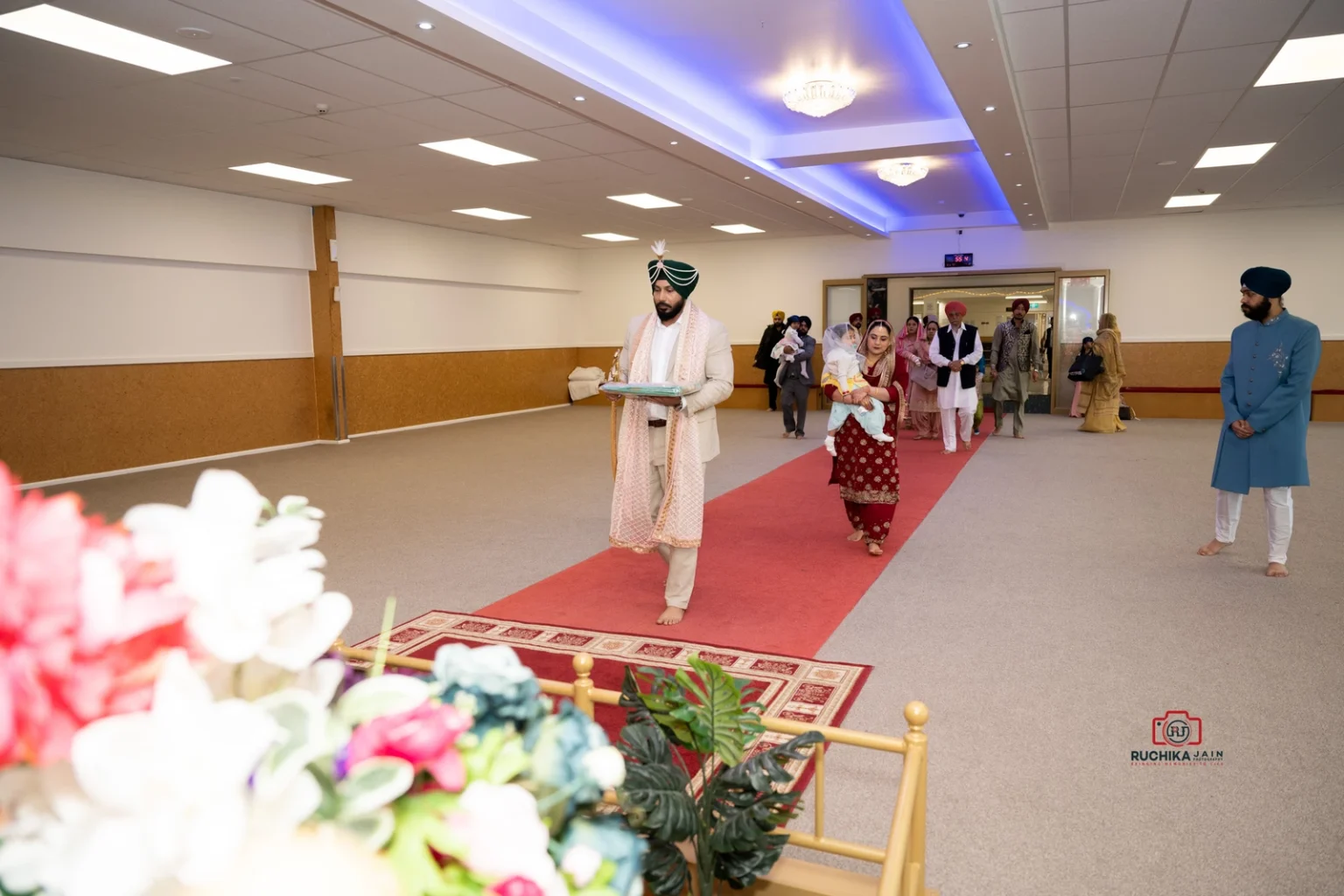 Sikh groom walking down a red carpet in a Gurdwara with family and friends following