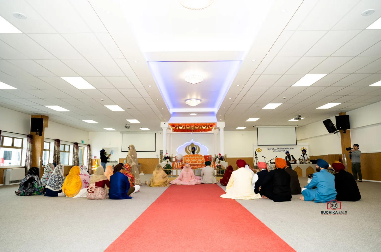 Sikh wedding ceremony at New Zealand Sikh Society Wellington with bride, groom, and guests seated facing the Guru Granth Sahib