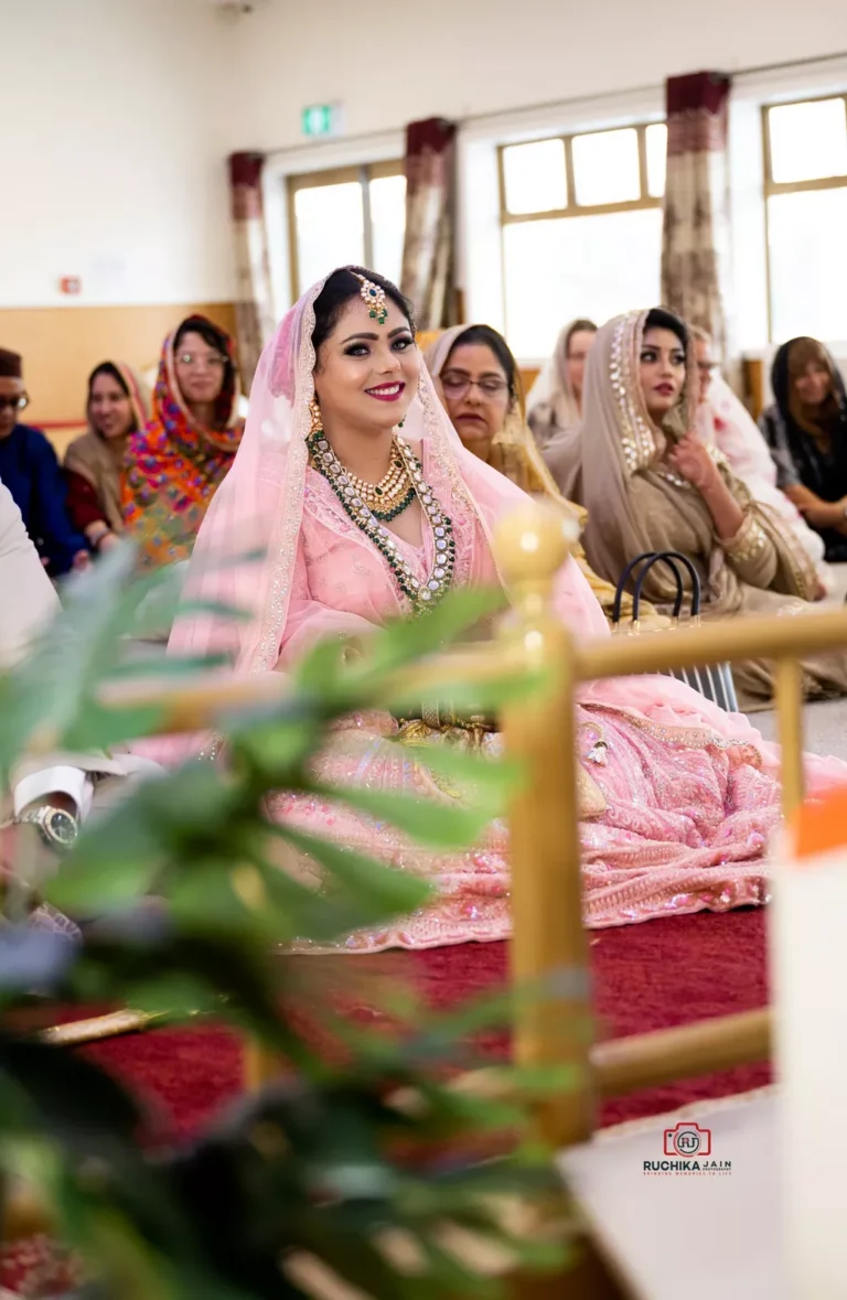 Smiling bride dressed in pink lehenga during a Sikh wedding ceremony, sitting among guests