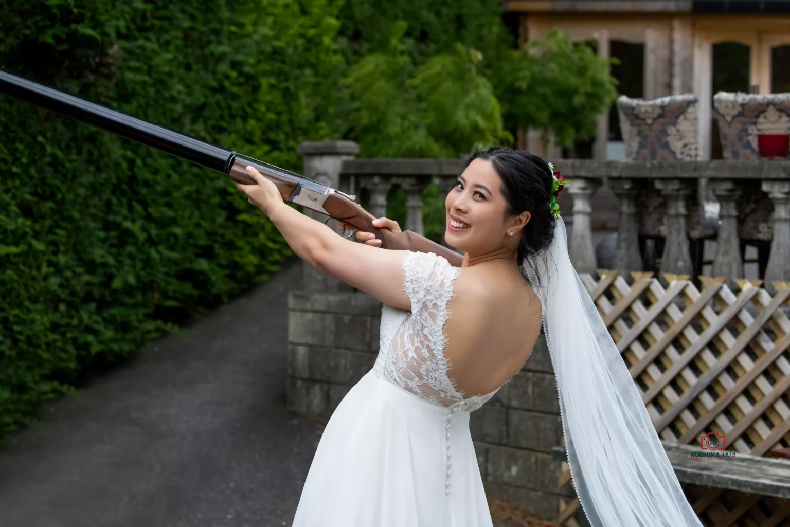 Smiling bride in a lace gown aiming a shotgun during an outdoor activity