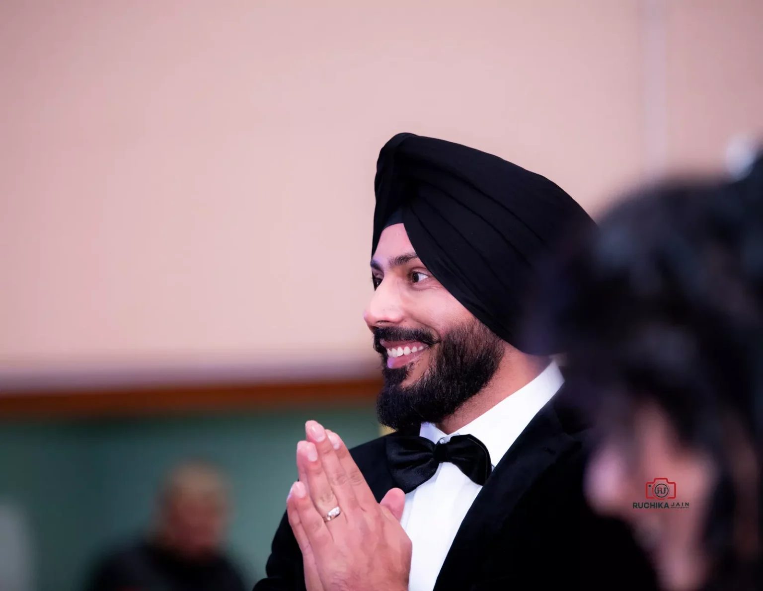 Smiling man in a black turban and tuxedo with folded hands during a formal event