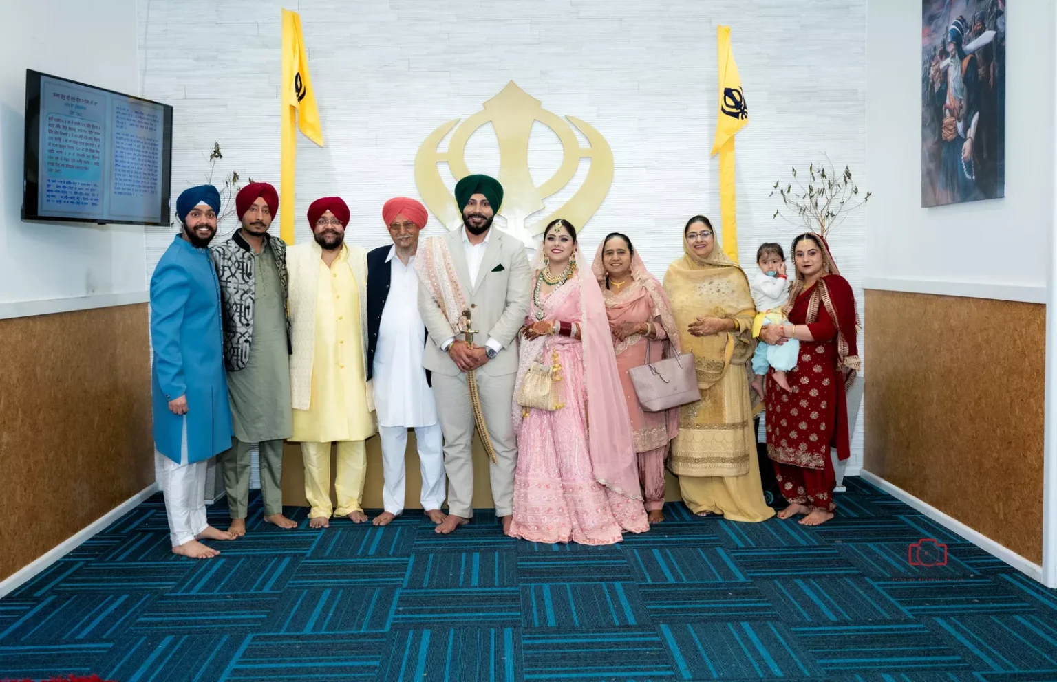 Wedding group photo with bride, groom, and family members standing together in a Sikh temple