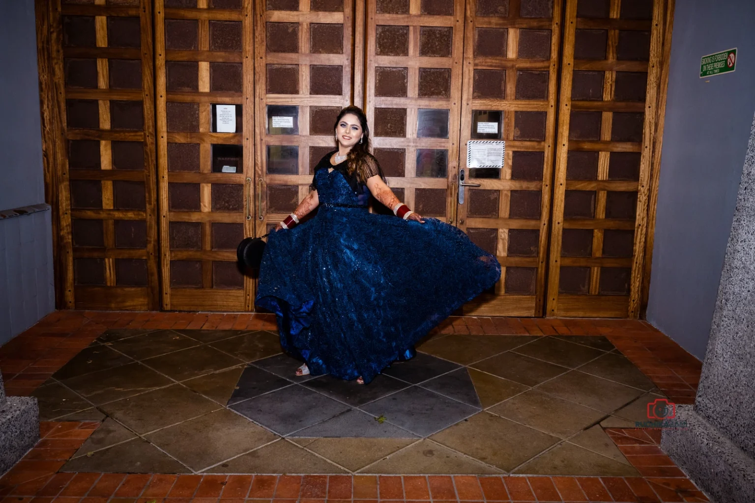 Woman in a dark blue gown posing while twirling outside a wooden door at night