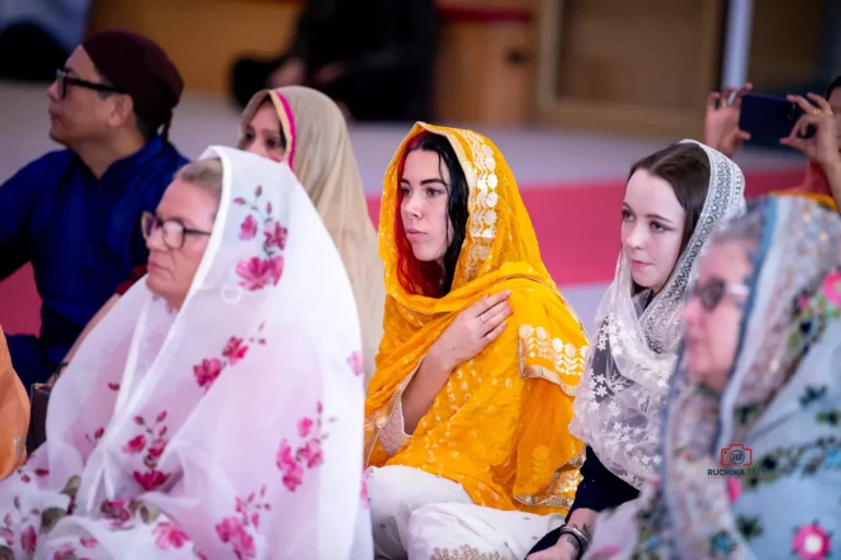 Women in colorful traditional scarves sit attentively during a Sikh wedding ceremony at a gurdwara