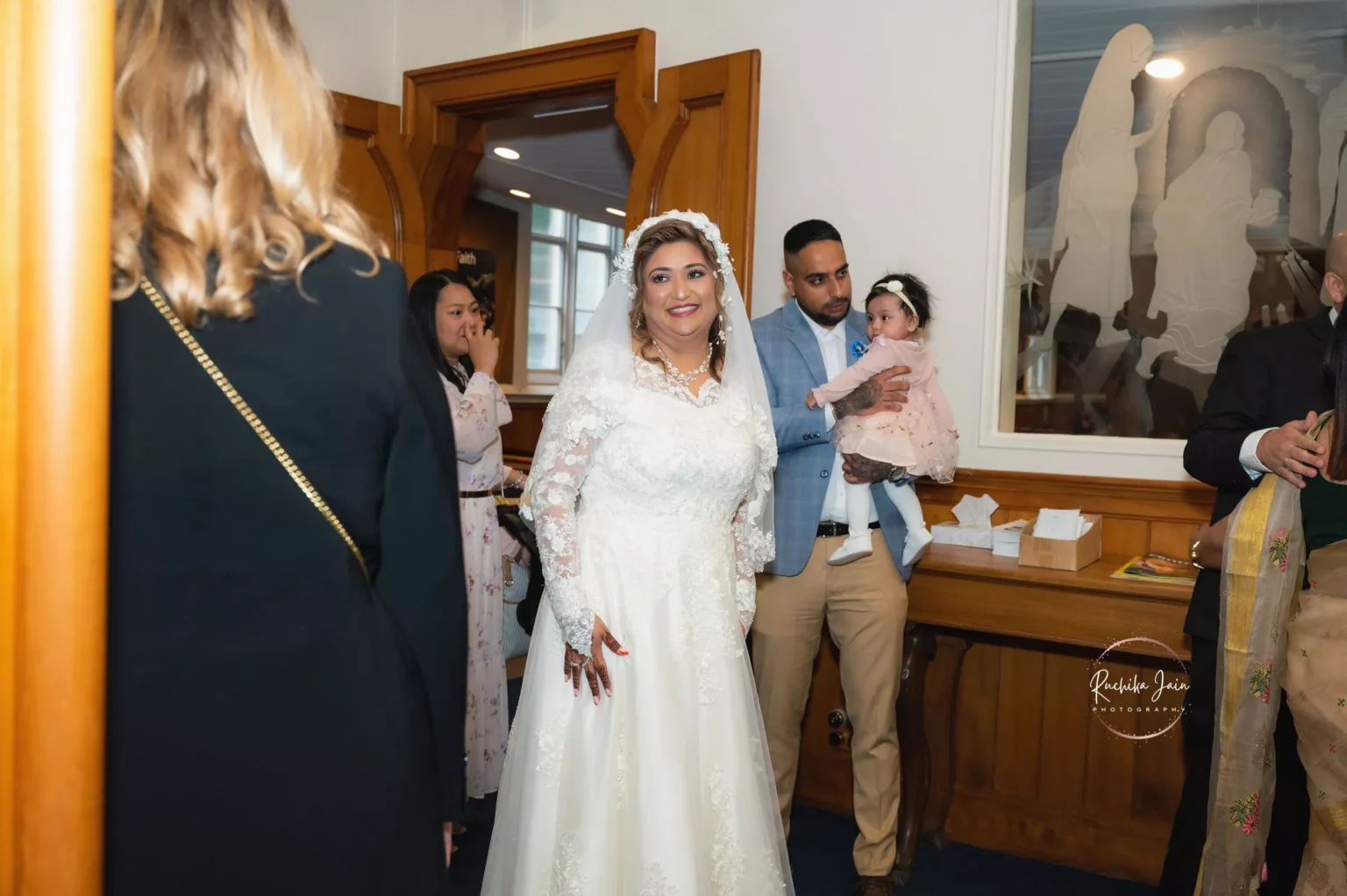 Smiling bride in a white wedding dress entering the church, surrounded by family and friends