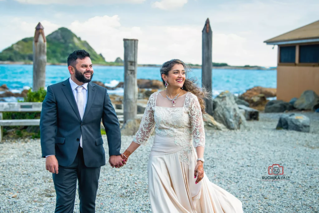 Bride and groom walking hand in hand by a scenic coastal venue with blue ocean and distant island in the background