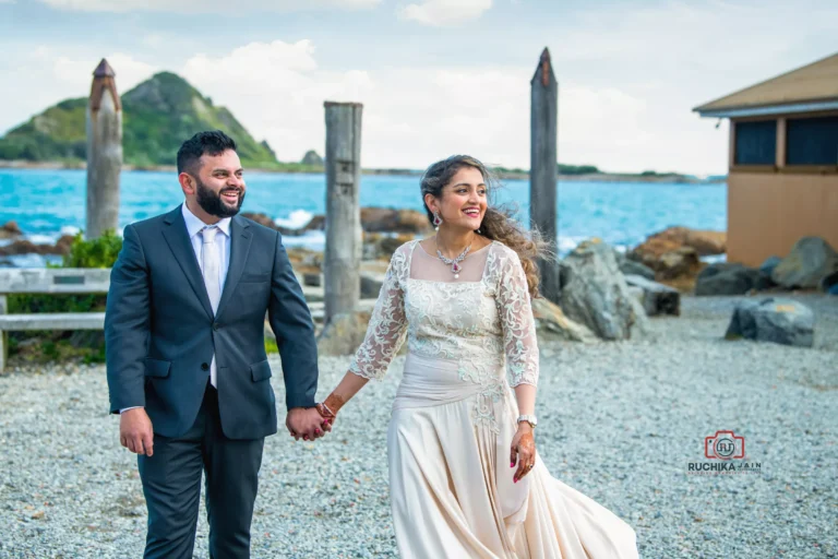 Bride and groom walking hand in hand by a scenic coastal venue with blue ocean and distant island in the background
