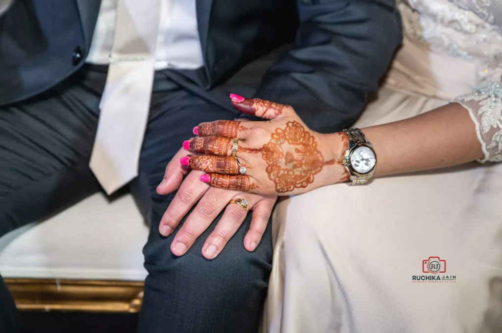 Close-up of bride and groom holding hands, showcasing the bride's henna design, rings, and watch at a Wellington wedding