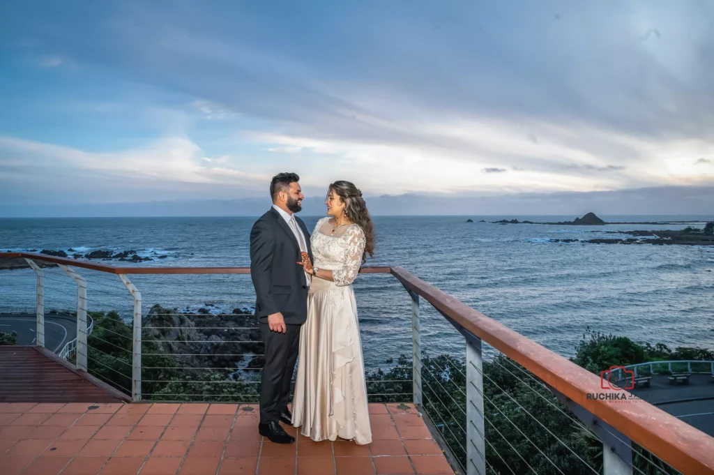 Bride and groom standing on a balcony overlooking the ocean at sunset in Wellington, New Zealand, sharing a romantic moment