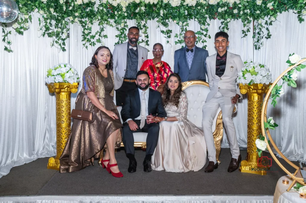 Bride and groom seated with family members at a wedding reception, surrounded by white floral decor and gold accents