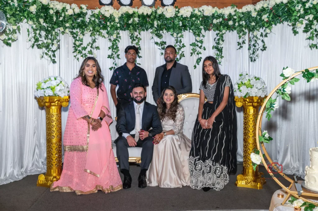 Bride and groom seated with friends and family members at a wedding reception, surrounded by elegant floral and gold decor