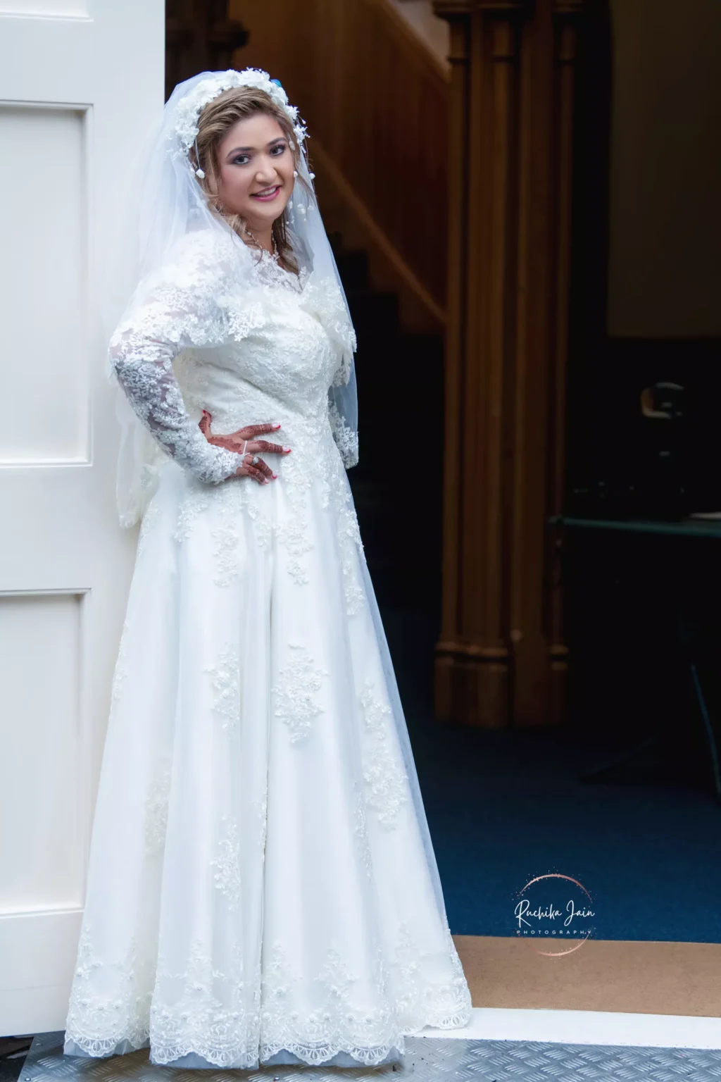 Bride in a lace wedding dress and veil, smiling and posing by a white doorway